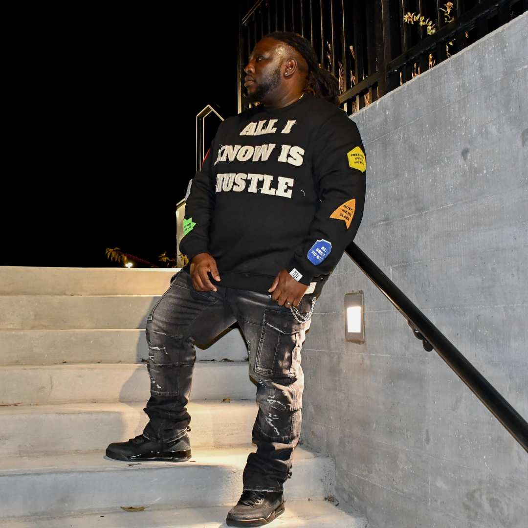 Man wearing a black sweatshirt with 'All I Know Is Hustle' text, standing on steps.