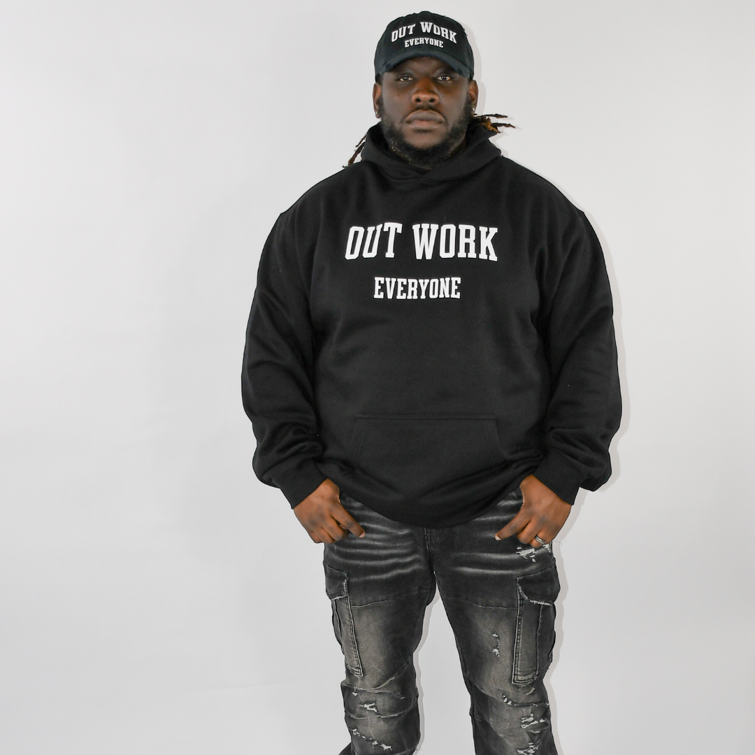 Person wearing a black hoodie with 'OUT WORK EVERYONE' text, standing against a plain background