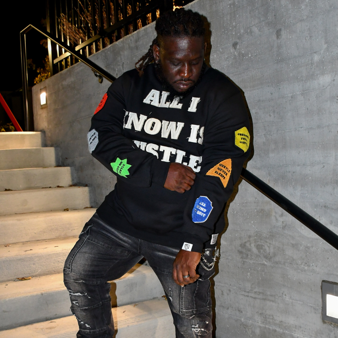 Person wearing a black sweatshirt with text and patches, sitting on stairs.