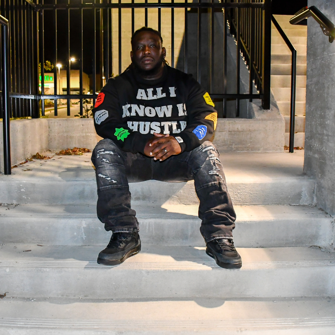 Person sitting on steps wearing a black sweatshirt with text and patches.