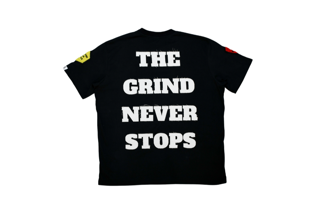 Black t-shirt with 'The Grind Never Stops' text on a white background